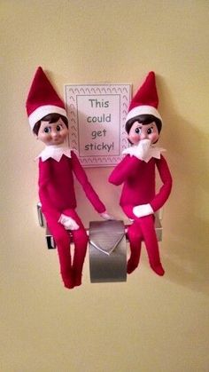 two elfs sitting on top of a toilet paper dispenser