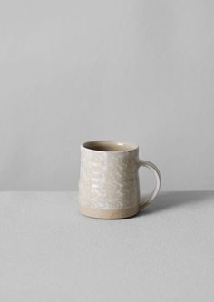 a white ceramic cup sitting on top of a gray countertop next to a wall