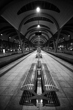 black and white photograph of benches in an empty train station with lights on the ceiling