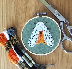 the scissors are next to an embroidery kit with a moth on it and several thread spools