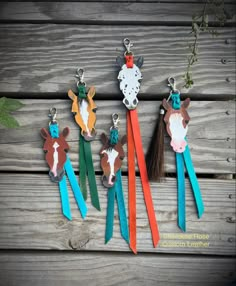 four different colored cow key chains hanging on a wooden fence with grass and flowers in the background