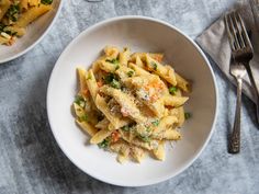 two bowls filled with pasta and vegetables on top of a table next to silverware