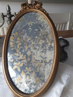 an ornate gold framed mirror sitting on top of a white table cloth next to a lamp