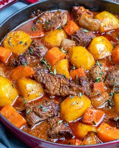 a pot filled with meat and vegetables on top of a blue table cloth next to a wooden spoon