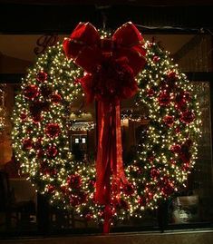 a large wreath with red bows and lights in front of a store window at night