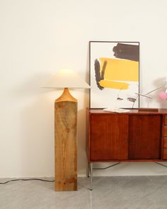 a lamp is sitting next to a wooden cabinet with a painting on the wall behind it