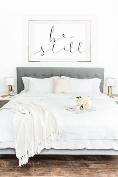 a white bed with two framed pictures above it and flowers on the end table next to it