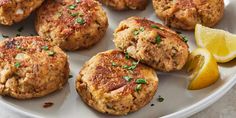 several crab cakes on a plate with lemon wedges