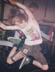 a young man is jumping in the air with his guitar while another guy watches from behind him