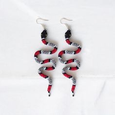 These handmade Scarlet Kingsnake Beaded Earrings are a striking statement piece inspired by the bold patterns of the scarlet kingsnake. Featuring intricate beadwork in red, black, and white, these unique earrings capture the beauty of nature and bring a bold, stylish touch to any outfit. Perfect for those who love snake-inspired jewelry, these earrings offer a blend of boho style and artistic craftsmanship. Whether as a standout accessory for yourself or a special gift for her, these earrings ar Adjustable Red Beaded Earrings With Black Beads, Red And Black Beaded Festival Earrings, Red And Black Beaded Earrings For Festival, Red Beaded Earrings With Black Round Beads, Earrings Snake, Beadwork Earrings, Special Gifts For Her, Snake Earrings, Christmas Deals