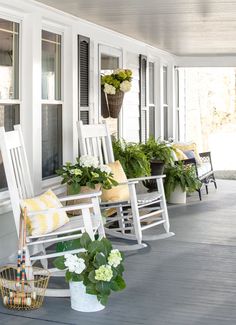 two white rocking chairs sitting on top of a porch next to flowers and potted plants