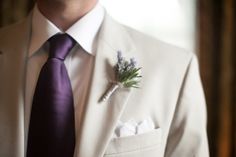 a man in a white suit with a purple tie and flower boutonniere