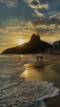 people walking on the beach at sunset with mountains in the backgrouund and clouds in the sky