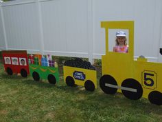 a child's train made out of cardboard sitting in the grass next to a white fence