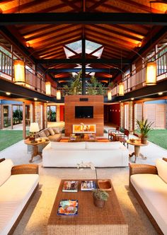 a living room filled with lots of furniture under a wooden roof over looking a lush green field