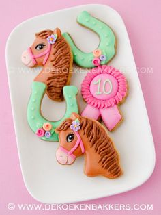 decorated cookies with horse heads and ribbons on a white platter against a pink background