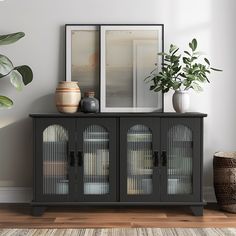 a black cabinet with glass doors and plants on top in front of a white wall