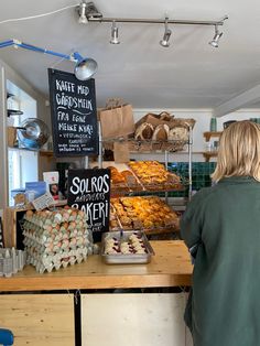 a woman standing in front of a counter filled with pastries and desserts at a bakery