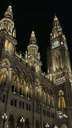 an ornate building lit up at night with clocks on the front and side of it