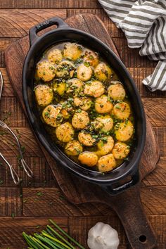 a skillet filled with cooked scallops on top of a wooden cutting board