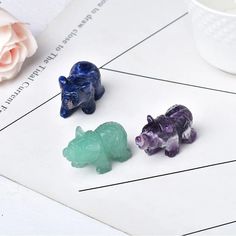 three small glass animals sitting on top of a table next to a cup and flower