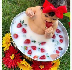 a baby sitting in a bowl of milk with strawberries on the side and flowers around it