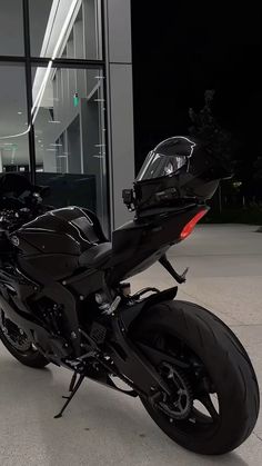 a black motorcycle parked in front of a glass building at night with its lights on