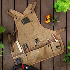 a tool bag sitting on top of a wooden table next to flowers and gardening tools