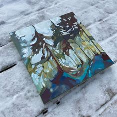 an abstract painting is displayed on the snow covered ground in front of some trees and bushes