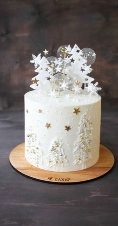 a white frosted cake with gold stars and trees on the top is sitting on a wooden platter