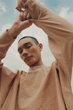 a man with his hands on his head and arms above his head, standing in front of a blue sky