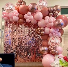 a woman sitting on a couch in front of a giant balloon arch with pink and gold balloons