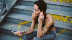 a woman sitting on the steps using her cell phone and looking at her wrist tattoo