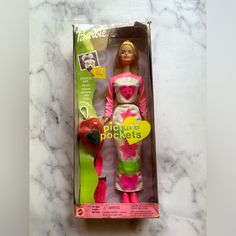 the barbie doll is in its box on the marble countertop, it's pink and green