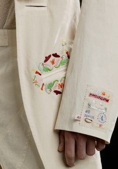 a person wearing a white suit and jacket with embroidered details on the lapel pocket