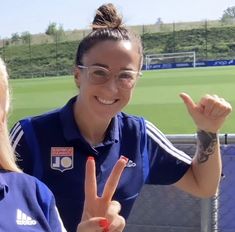 two women are making the peace sign at a soccer game in front of an empty field