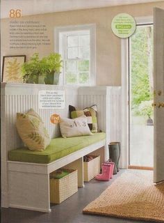 a white bench with green cushions in front of a door and window on the wall