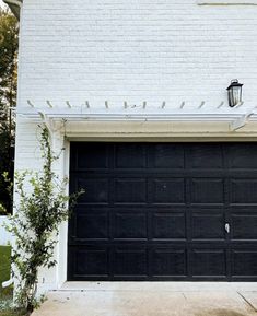 a white brick building with a black garage door and light on the side of it