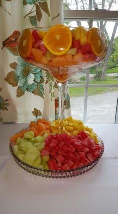 a platter filled with sliced up fruit on top of a white table next to a window