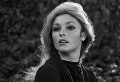 black and white photo of a woman in front of some bushes looking at the camera