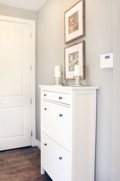 a white dresser with two framed pictures on the top and bottom, in front of a door