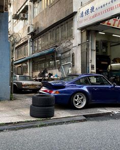 a blue car parked in front of a building next to a tire on the street