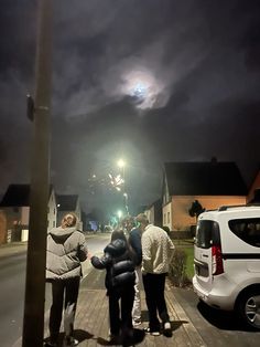 three people are standing on the sidewalk at night with fireworks in the sky behind them