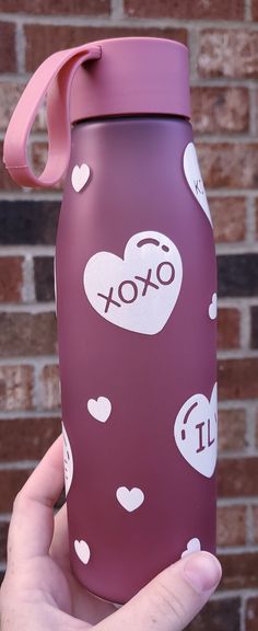 a hand holding a purple water bottle with hearts on it