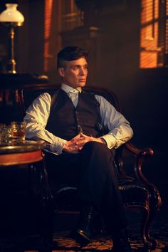 a man sitting in a chair wearing a vest and tie with his hand on his hip