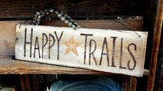 a wooden sign that says happy trails hanging on a shelf with other items in the background