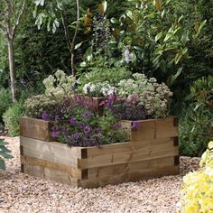 a wooden planter filled with lots of flowers and greenery next to trees in the background