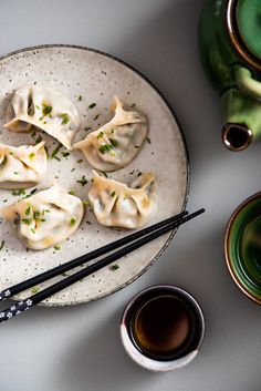 some dumplings are on a plate with chopsticks and a cup of tea