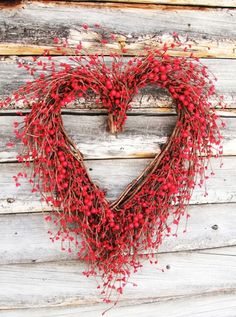 a heart shaped wreath with red berries hanging on the side of a wooden wall,