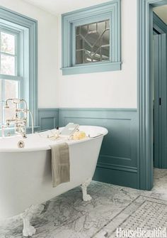 a white bath tub sitting next to a window in a bathroom with blue trim on the walls